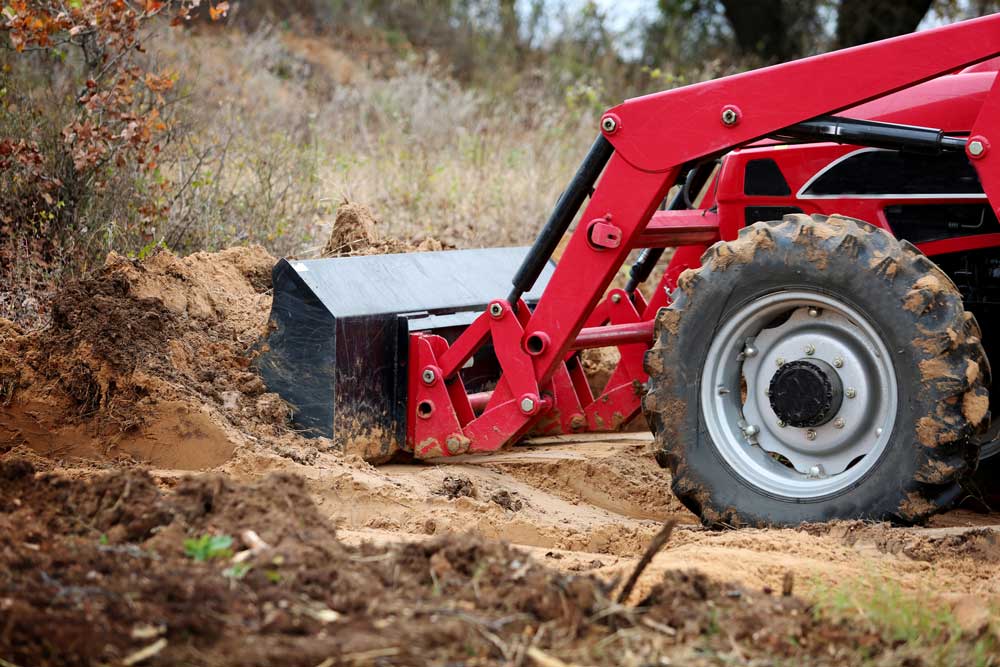 En röd grävskopa gräver upp mark på en skogsväg