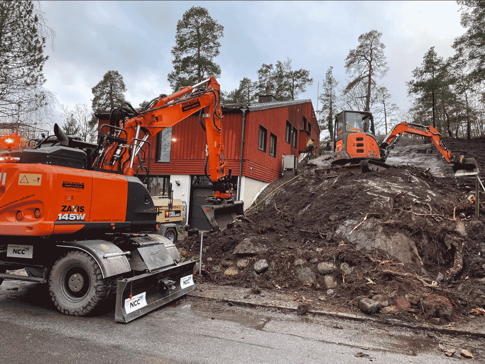 En gul grävskopa gräver upp mark på en skogsväg